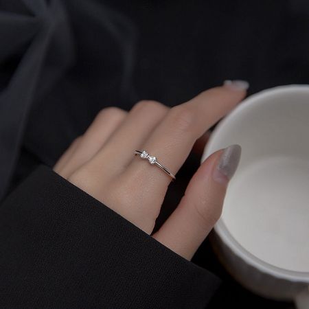 A detailed view of the dainty silver bow ring on a finger.