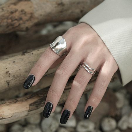 A hand model showcasing the sterling silver wave ring stacked with other minimalist rings, highlighting its versatility.