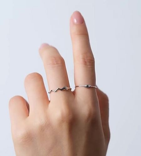 Model wearing two sterling silver wavy rings on her middle and ring fingers.