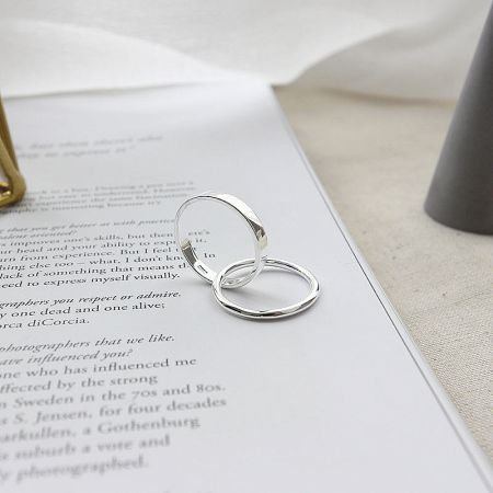 Two stacked 925 sterling silver rings with a minimal loop design resting on the pages of a book.