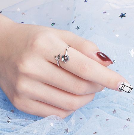 Model's hand wearing multiple sterling silver rings from the mermaid tail collection against a soft blue background.