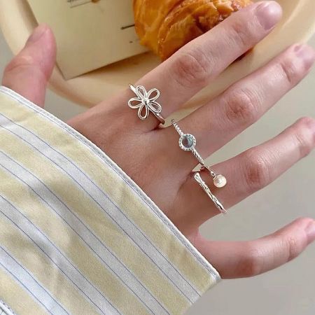 Two adjustable silver rings, one with a delicate flower and the other with a twisted band and pearl.