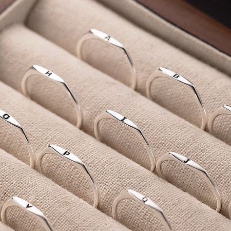 A collection of 925 sterling silver letter rings elegantly arranged in a beige jewelry box.