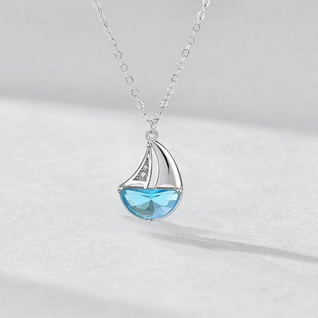 The sailboat pendant necklace shown against a neutral background to highlight the vibrant blue gemstone.