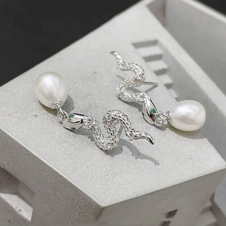 Full view of the pair of silver snake pearl earrings with green gemstone eyes.