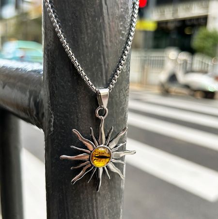 Detailed view of the silver sunburst pendant with its vibrant yellow gemstone center.
