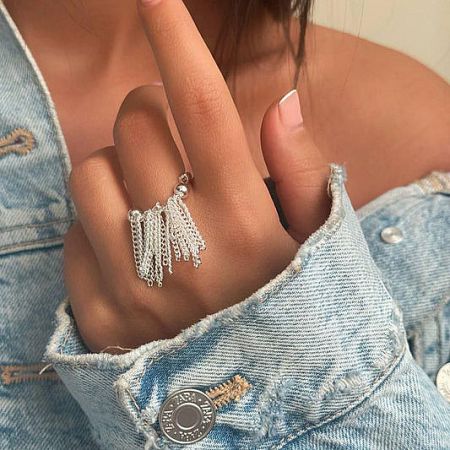 Elegant stainless steel ring with a delicate silver tassel charm, worn on a model's hand.