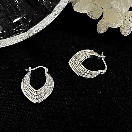 Another perspective of the silver layered shield earrings against a light background.