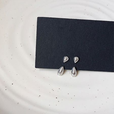 Close-up of the silver drop shape ear studs on a display card.