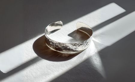 A close-up of a polished silver cuff bracelet with a unique hammered texture.