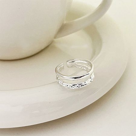 Close-up of a textured sterling silver adjustable ring from the set, placed on a white ceramic saucer.