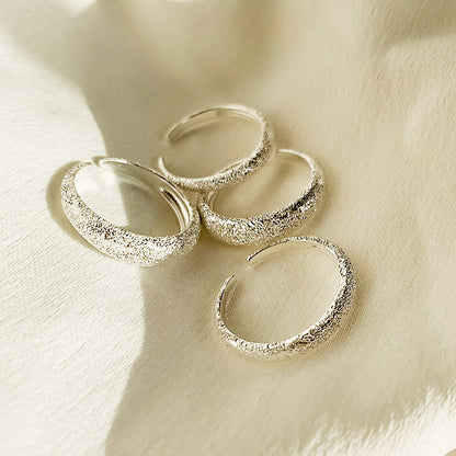A collection of four sterling silver frosted open rings displayed on a textured cream surface.