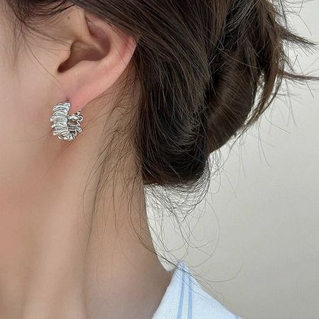 Close-up of a woman wearing the irregular pleated C-shaped silver hoop earring, showcasing its fit and style.