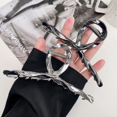 A hand holding two silver hair clips, highlighting their unique twisted design and metallic sheen.
