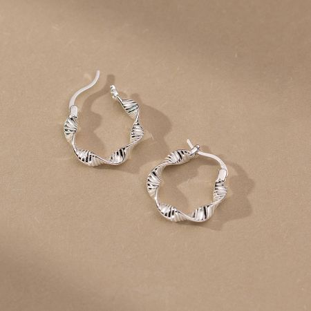 Studio shot of the twisted silver hoop earrings against a clean, beige background.