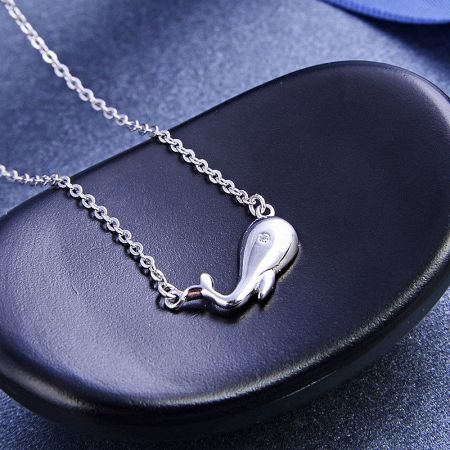 The silver whale necklace displayed elegantly on a black leather case.