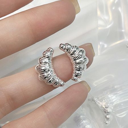 A hand holding the croissant-shaped silver earrings to show scale and detail.