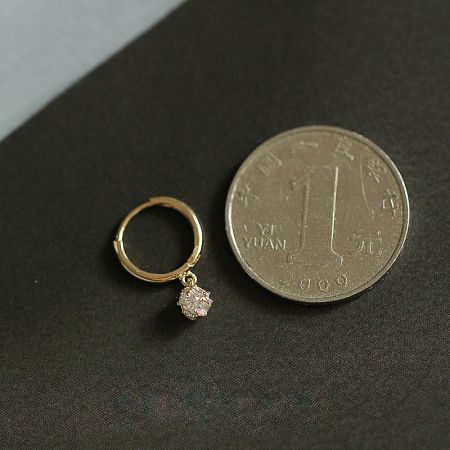 A small gold earring with a sparkling diamond charm, shown for scale.