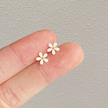 The small white daisy flower earrings held between fingers to show their miniature scale.