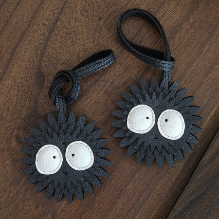 Two Soot Sprite PU leather charms displayed on a wooden surface, highlighting the product set.