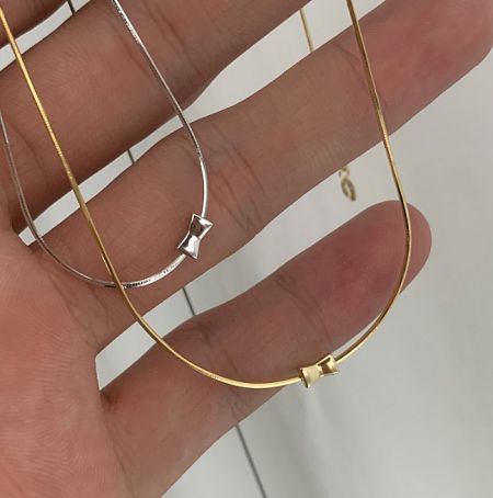 925 Sterling Silver Chain Necklace - A hand holding two delicate 925 sterling silver chain necklaces, one in silver and one in gold, each adorned with a small star pendant. Available for wholesale from JR Fashion Accessories.