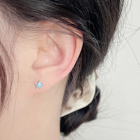 Close-up view of the tiny blue enamel starfish stud earring being worn.