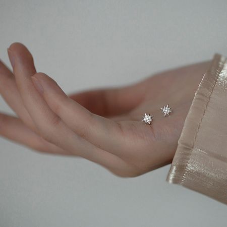 A pair of starburst earrings held in hand to show scale.