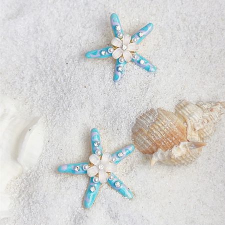 The starfish earrings displayed on a bed of sand with seashells, highlighting their ocean theme.