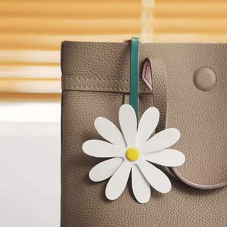 Close-up of a white PU leather flower charm on a tan handbag.