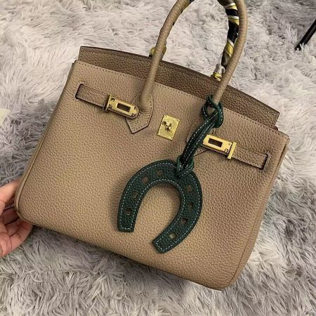 Green leather horseshoe charm attached to a tan luxury handbag.