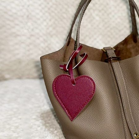 A close-up of a red heart-shaped leather charm attached to a classic tan handbag.