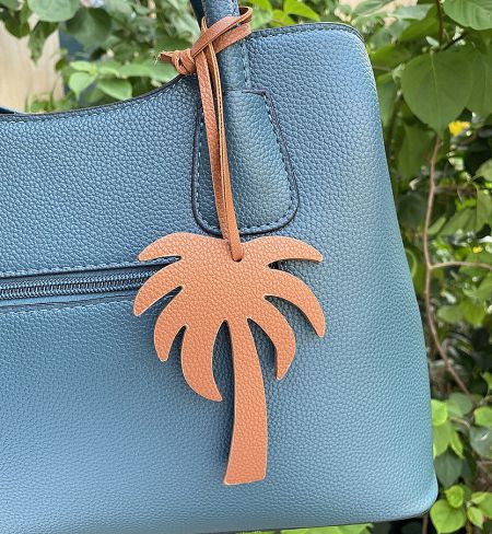 A brown leather coconut tree keychain complementing a teal blue handbag.