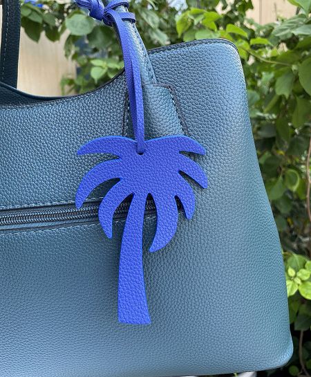 A blue coconut tree leather keychain adding a pop of color to a teal handbag.