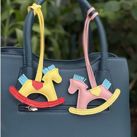 Two rocking horse charms, yellow and pink, decorating the front of a teal handbag.
