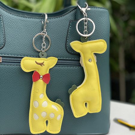 A stylish teal leather handbag accessorized with two charming yellow giraffe keychains.