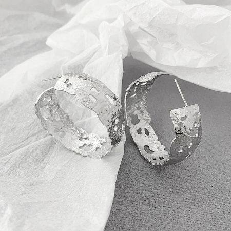 Side view of a textured metal hoop earring, highlighting its chunky, hammered design and craftsmanship.