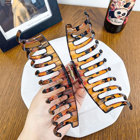 A hand holding open a tortoiseshell hair clip to demonstrate its size and grip.