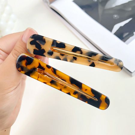 A hand holding two classic tortoiseshell pattern duck beak hair clips.