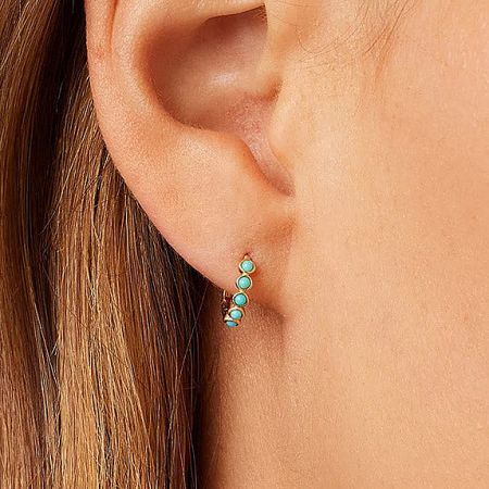 Close-up view of a classic turquoise huggie hoop earring worn on an ear.