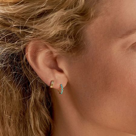 Detailed shot showcasing a gold hoop and a dangling turquoise stone earring.