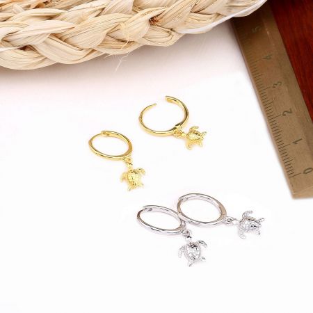 Both gold and silver turtle huggie earrings displayed together.
