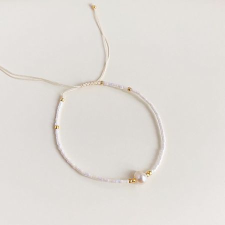 An elegant white beaded bracelet with an adjustable clasp, gold accents, and a pearl.
