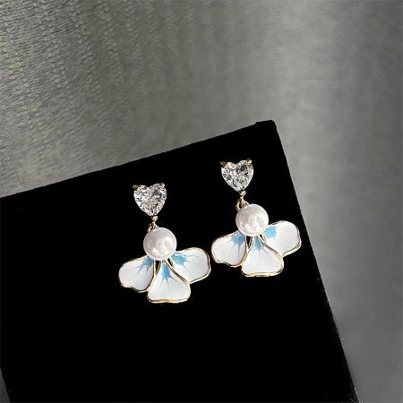 Close-up of the white and blue enamel flower earrings with brilliant gold accents and a central pearl.