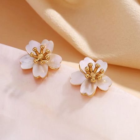 Elegant white flower earrings with gold details on a soft pink background.