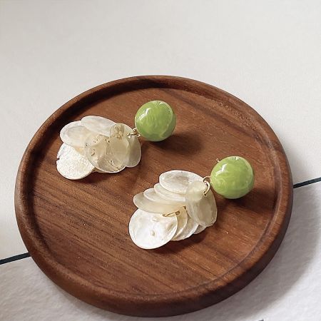 A pair of floral design earrings with white mother-of-pearl petals and green beads, displayed on a wooden plate.