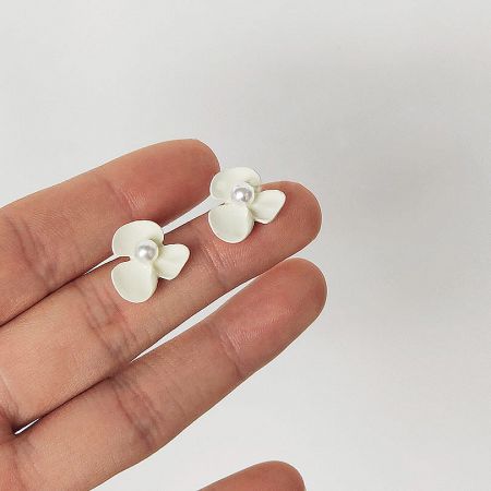 Elegant Small White Flower with Pearl Stud Earrings (5 pairs) - A close-up of the Elegant Small White Flower with Pearl Stud Earrings, held between fingers to show their delicate size and detail. The brass earrings feature white petals and a central pearl.