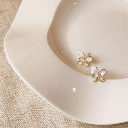 Top-down view of the pair of white and gold butterfly earrings with pearls on a white plate.