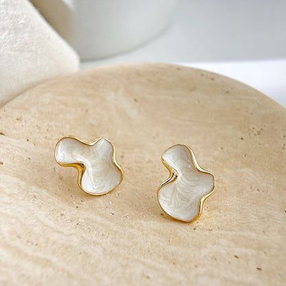 The unique white and gold earrings presented on a textured beige stone for a natural aesthetic.