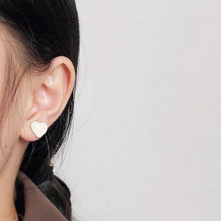 Side view of a woman wearing a delicate white enamel heart-shaped stud earring.
