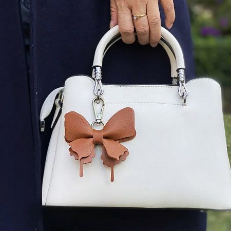 Brown faux leather bow charm attached to a white handbag.
